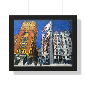 Puede incluir: Impresión artística enmarcada de una escena de la calle de la ciudad. La obra representa edificios altos en tonos marrones, amarillos y blancos, con un cielo azul profundo. También se ven una farola y banderas, con gente caminando debajo.