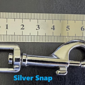 May include: A silver-coloured metal swivel snap hook positioned below a metal ruler. The snap hook measures approximately 8.2 cm in total length. The text "Silver Snap" is printed in blue below the metal hardware component.