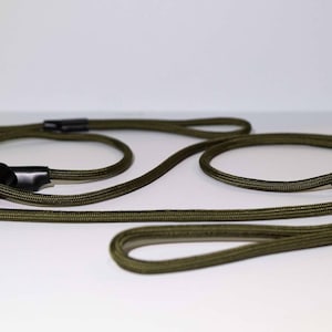 Pode incluir: Uma trela de corda verde-azeitona com dois la&ccedil;os ajust&aacute;veis e deslizadores de pl&aacute;stico preto. O cord&atilde;o &eacute; feito de um material entran&ccedil;ado e o design inclui v&aacute;rios la&ccedil;os integrados para um manuseamento seguro e pontos de fixa&ccedil;&atilde;o.
