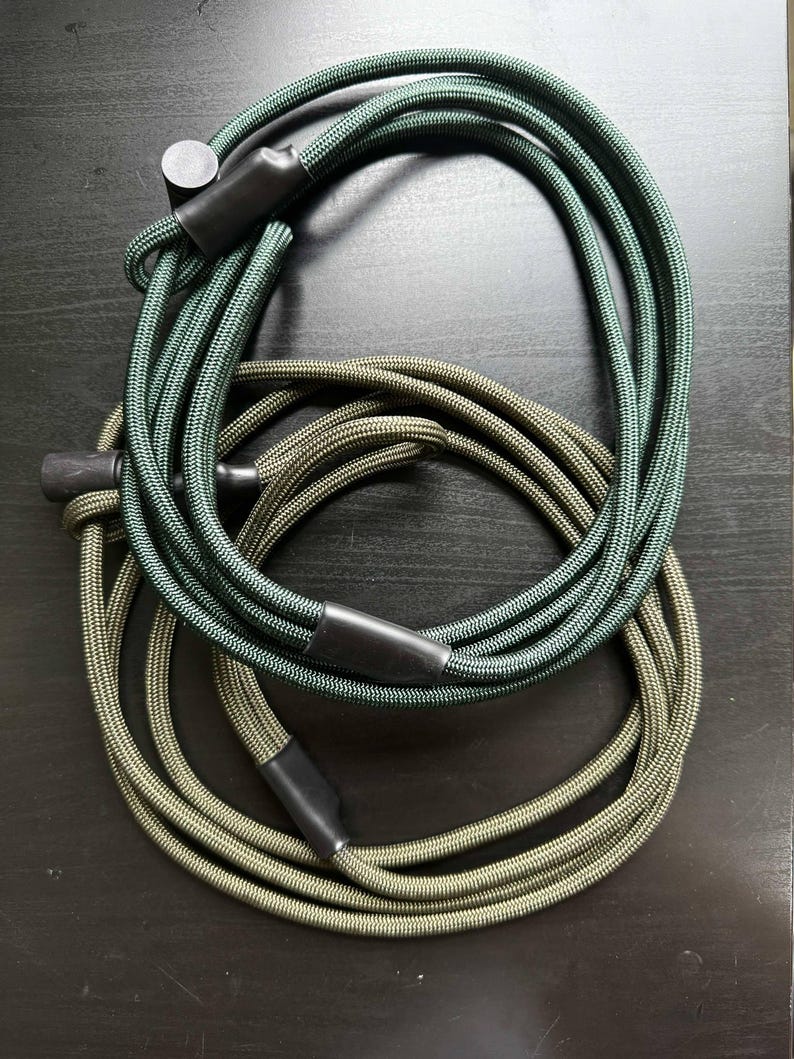 Pode incluir: Dois comprimentos de corda tran&ccedil;ada enrolados, um em verde floresta profundo e o outro em verde oliva suave. Cada corda apresenta pontas cil&iacute;ndricas pretas lisas e um mecanismo deslizante de pl&aacute;stico preto para ajustar o comprimento do cord&atilde;o.