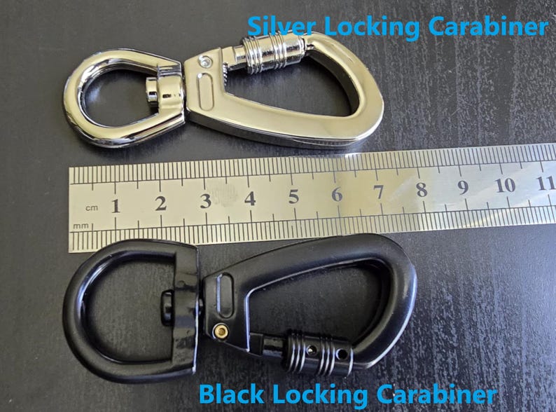 May include: A silver locking carabiner and a black locking carabiner positioned next to a metal ruler. The silver carabiner measures approximately 3 inches in length, while the black carabiner measures approximately 3 inches in length.