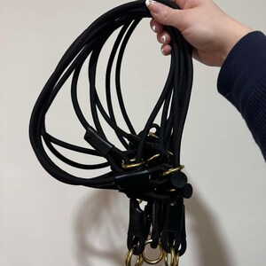May include: A collection of black rope leads featuring gold-toned metal rings and black leather-like connectors. The ropes are flexible and looped, with multiple segments joined together by circular hardware, creating a functional design.