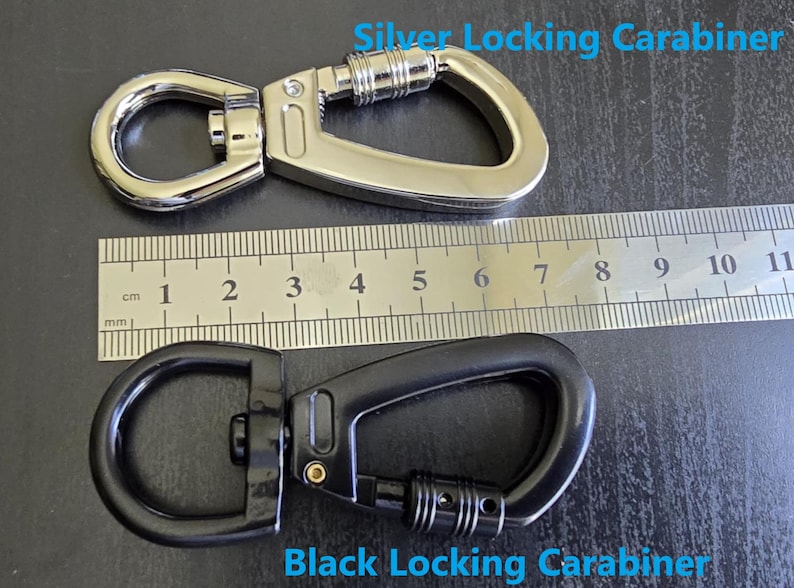 May include: A silver locking carabiner and a black locking carabiner, each featuring a swivel eyelet and a screw-gate mechanism. A metal ruler is positioned between the two carabiners, showing a length of approximately 9 cm for each item.