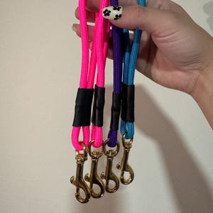 Peut inclure: Quatre dragonnes en corde de nylon tress&eacute;e de couleur rose fluo, violette et bleu vif. Chaque dragonne est dot&eacute;e d'un connecteur en gaine thermor&eacute;tractable noire et d'un mousqueton pivotant en m&eacute;tal dor&eacute; &agrave; la base pour attacher des objets.