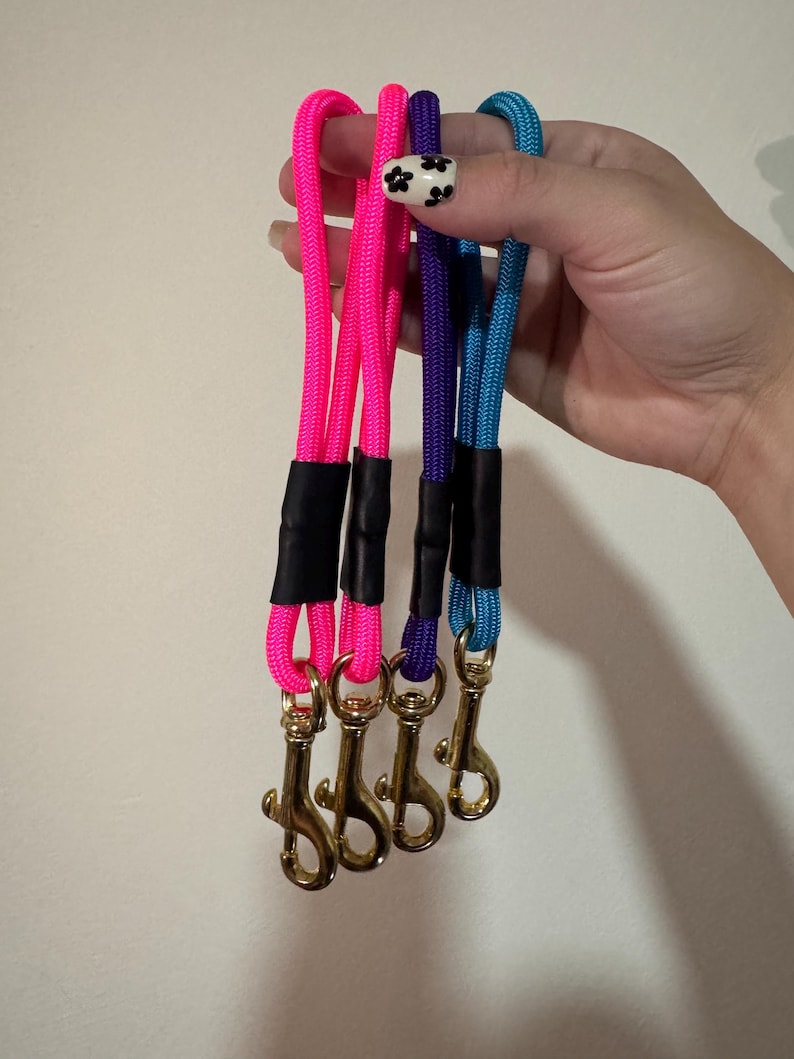 Peut inclure: Quatre dragonnes en corde de nylon tress&eacute;e de couleur rose fluo, violette et bleu vif. Chaque dragonne est dot&eacute;e d'un connecteur en gaine thermor&eacute;tractable noire et d'un mousqueton pivotant en m&eacute;tal dor&eacute; &agrave; la base pour attacher des objets.