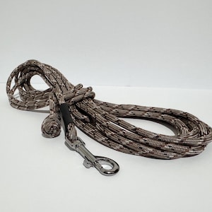 May include: A coiled dog leash in a brown and gray camouflage pattern. The leash has a metal clasp and a black connector. The rope is tightly woven and appears durable. The leash is designed for pet owners.