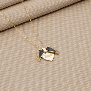 May include: A gold chain necklace with a heart-shaped pendant featuring black wings and the word "Angel" engraved on it.
