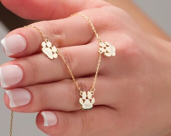 May include: Gold necklace with three paw print charms. Each charm is engraved with a different name: "Max", "Charlie", and "Winston".