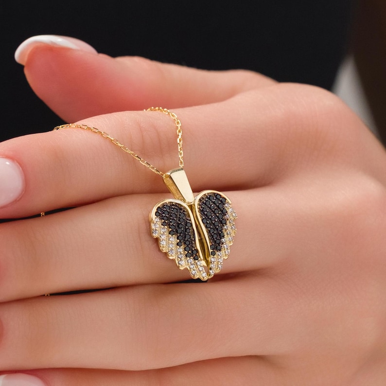 May include: A gold necklace with a heart-shaped pendant featuring black and white cubic zirconia stones arranged in a wing design.