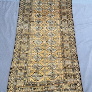 Puede incluir: Una alfombra rectangular, tejida a mano, con un campo central de color amarillo dorado y patrones geométricos intrincados en negro y gris. La alfombra tiene un borde oscuro y un borde con flecos, mostrando un diseño tradicional.