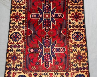 Puede incluir: Una alfombra rectangular tejida a mano con un campo central rojo y intrincados patrones geométricos. El diseño presenta detalles en azul marino y beige, con un borde de motivos repetidos. Los bordes de la alfombra tienen un acabado con flecos.