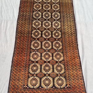 Puede incluir: Alfombra rectangular con un diseño geométrico en tonos marrón, naranja y beige. El diseño central presenta formas octogonales repetidas, enmarcadas por un borde con un patrón detallado y repetitivo. La paleta de colores de la alfombra crea una estética cálida y acogedora.