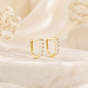 May include: A pair of gold hoop earrings featuring a U-shaped design. Each earring is accented with four small, round, iridescent white opal stones set in a vertical row along the outer edge of the hoop, secured by small gold prongs.