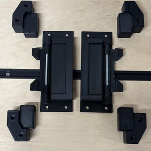 May include: Black hardware set for a cabinet or chest, including hinges, latches, and corner brackets. The set is arranged on a light wood surface, providing a contrast to the dark components. The hardware appears to be new and unused.