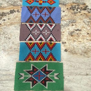 May include: A set of eight beaded strips with various geometric patterns in shades of blue, green, red, yellow, black, and white. The strips are arranged vertically, with the green strip at the bottom.