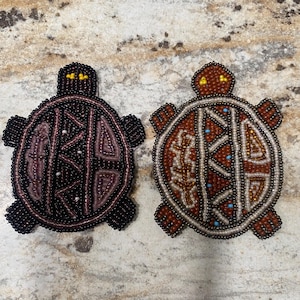 May include: Two beaded turtle ornaments, one with a brown and white design and the other with a purple and black design.