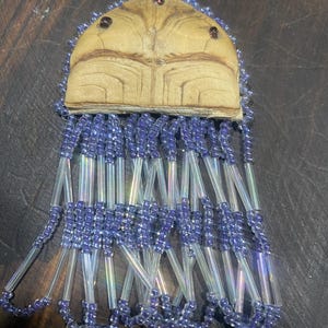 May include: A beaded Native American pendant with a carved wooden top and a fringe of purple and clear beads.