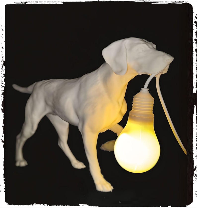 以下が含まれることがあります： 白いセラミック製の犬の彫刻が点灯した電球を持っています。犬は黒い表面の上に立っています。