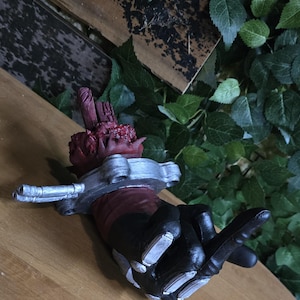 Può includere: Una mano robotica nera e argentata con un braccio meccanico rosso e argentato. La mano sta facendo un gesto di dito medio.
