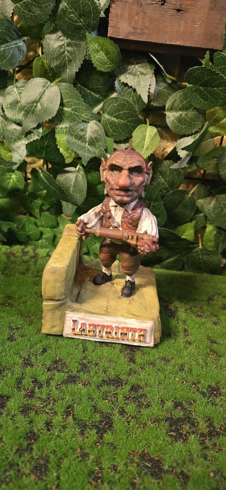 May include: A detailed figurine of a character from the film Labyrinth. The figure is brown and tan, holding a club, and standing on a base with the word "Labyrinth" on it. The background is green.