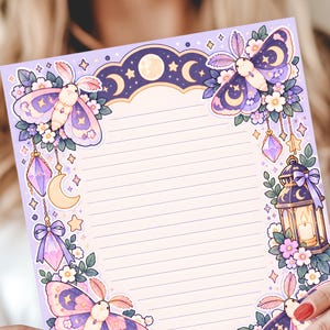 May include: A sheet of light purple stationery with horizontal lines, featuring illustrations of moths, flowers, crystals, a lantern, and a moon phase arch at the top. The design includes soft pink, purple, and yellow colour accents throughout.