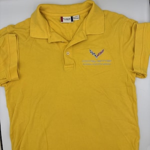 May include: A yellow polo shirt with short sleeves. The shirt has a collar and a three-button placket. The left chest features a logo with the text "CORVETTE NATIONAL CONVENTION". The brand label "CLIQUE" is visible on the collar.