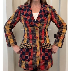 May include: A long-sleeved blazer featuring a textured, woven plaid pattern in shades of navy blue, mustard yellow, and red. The garment includes a notched lapel, three front buttons, and two large patch pockets with a contrasting houndstooth trim.