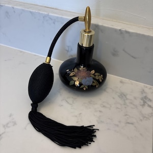 May include: A black vintage perfume bottle with a gold-colored top and floral design. The bottle has a black bulb atomizer with a tassel. The perfume bottle is a decorative item.