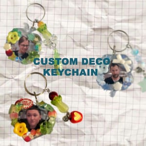 Könnte beinhalten: Drei individuelle Deko-Schlüsselanhänger mit Fotos und farbenfrohen Verzierungen. Jeder Schlüsselanhänger zeigt das Foto einer anderen Person, umgeben von Blumen, Früchten und Perlen. Der Text "CUSTOM DECO KEYCHAIN" ist zu sehen.