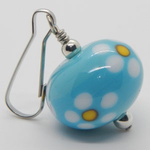 May include: Blue glass bead earrings with white and yellow daisy print. The earrings have silver hooks.