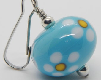 May include: Blue glass bead earrings with white and yellow daisy print. The earrings have silver hooks.