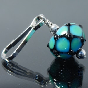 May include: A silver metal clip with a blue and black glass bead. The bead has a geometric pattern with black accents.