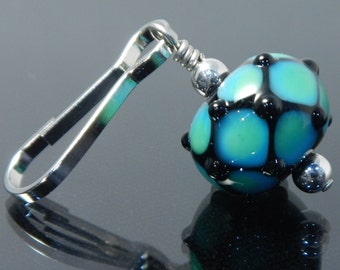 May include: A silver metal clip with a blue and black glass bead. The bead has a geometric pattern with black accents.