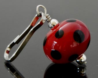 May include: A red and black glass bead with a silver clip. The bead is decorated with black polka dots.