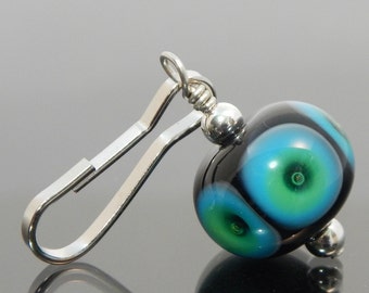 May include: A black glass bead with blue and green eye-like patterns, attached to a silver clip.