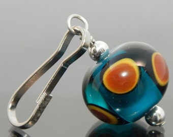 May include: A teal blue glass bead with orange and black accents hangs from a silver metal loop. The bead has a shiny, glossy finish.