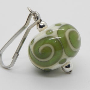 May include: A green and white glass bead with a swirl pattern, attached to a silver metal clasp.