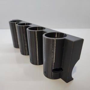 May include: A gray 3D printed holder with four cylindrical slots. The holder is designed to hold small objects, such as pens or pencils.