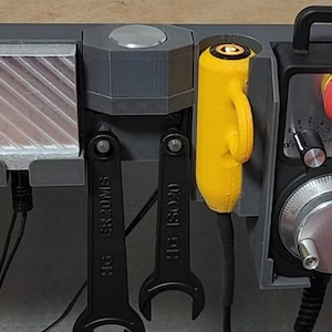 May include: A gray wall-mounted organizer with a red button, a yellow tool, two black wrenches, and a gray knob. The wrenches are labeled "FIT" and "SECONDS".