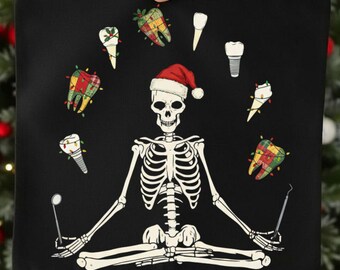 May include: Black square cushion featuring a skeleton in a Santa hat, surrounded by teeth with fairy lights. The skeleton is holding dental tools. Festive dental-themed design.