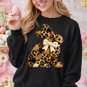 Può includere: Felpa nera con un design a coniglio patchwork. Il coniglio presenta un motivo leopardato e un fiocco color crema. Il design è realizzato con varie toppe di tessuto. La felpa è uno stile girocollo, adatta per Pasqua o primavera.