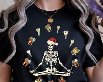 May include: Black t-shirt with a skeleton in a Santa hat, in a yoga pose, surrounded by cartoon teeth with festive lights. The teeth have plaid and colourful designs. A gold necklace is visible.