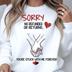 May include: White sweatshirt featuring the red text "SORRY" and the black text "NO REFUNDS OR RETURNS...". Below, two hands are clasped, with the names "James" and "Jennifer" written on them. The phrase "YOU'RE STUCK WITH ME FOREVER" is at the bottom, with heart graphics.