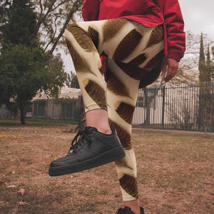 May include: A person wearing black sneakers and leggings with a brown and white feather pattern. The leggings are worn with a red jacket.