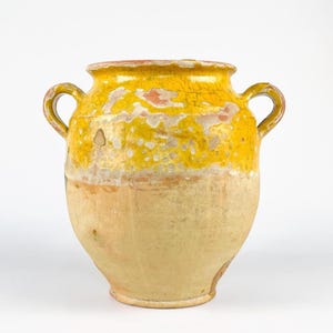 May include: A rustic earthenware vessel featuring two side handles and a wide mouth. The upper portion is finished with a vibrant yellow glaze that shows significant wear and cracking, while the lower section remains an unglazed, matte tan.
