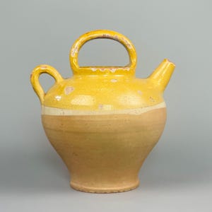 Peut inclure: Pichet en céramique jaune avec une anse et un bec verseur. Le pichet a un corps arrondi et une bande jaune plus claire au milieu. La poignée est arquée et il y a une petite anse sur le côté. Le pichet mesure environ 25 cm de haut.