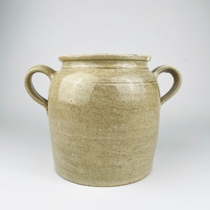 Può includere: Un vaso in ceramica beige con finitura maculata e due manici laterali. Il recipiente presenta un corpo cilindrico largo con un bordo leggermente svasato e una superficie liscia e smaltata. Il design è semplice, essenziale e funzionale.