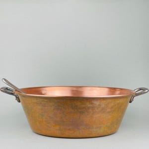 May include: A large, copper pot with two handles. The pot has a worn, aged patina and is likely used for cooking or making candy.