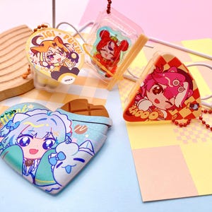 Puede incluir: Un surtido de coloridos llaveros de estilo anime y una funda en forma de corazón. Los llaveros presentan personajes de dibujos animados en varias formas, incluyendo un círculo, un cuadrado y un triángulo. La funda en forma de corazón tiene un diseño de barra de chocolate.