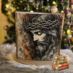 May include: A black and white illustration of a man with a crown of thorns on his head. The image is on a wooden panel with a brown background.